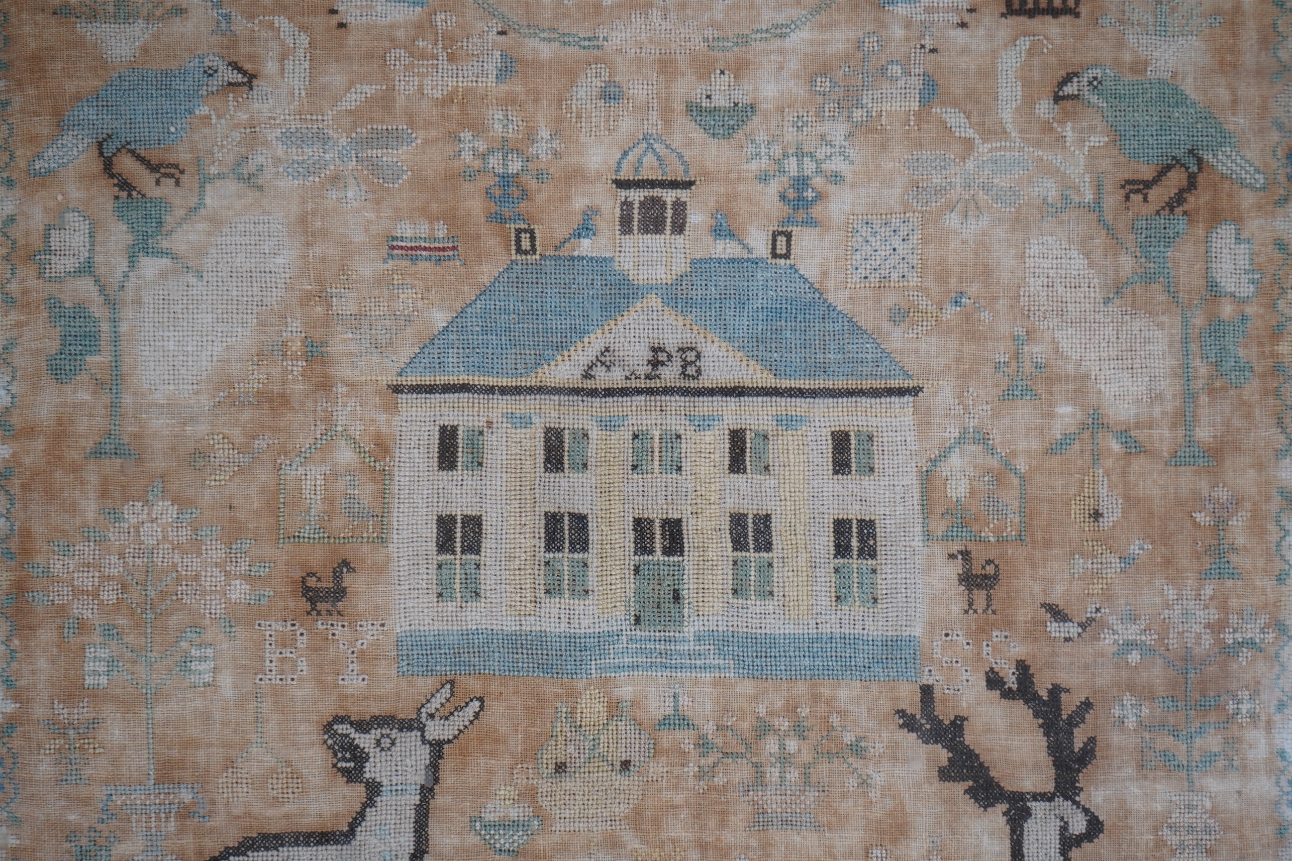 A framed 18th century sampler, dated 1779 by SS., worked in fine cross stitch with motifs of angels, figures, flowers, trees birds a fox and a stag surrounding a house with initials APB. 39cm x 37.5cm. Condition - the em
